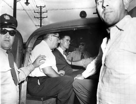 Howard Unruh (in suit and bowtie) placed into custody minutes after calmly murdering 13 people in Camden, NJ in 1949.